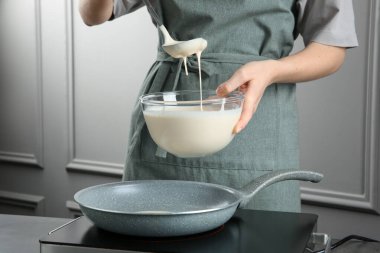 Mutfaktaki gri masada kaseden tavaya sıvı hamur döken kadın, yakın plan.