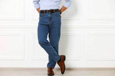 Beyaz duvarın yanında şık kotlu adam, yakın plan.