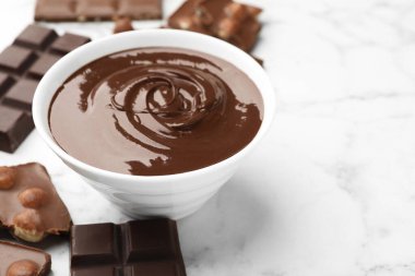 Erimiş çikolata ve parçalarla dolu bir kase beyaz mermer masa, yakın plan. Metin için boşluk