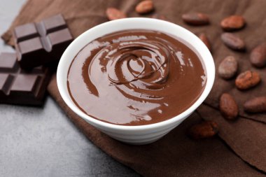 Erimiş çikolatalı kase, fasulye ve parçalar gri masada, yakın plan.