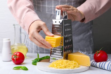 Beyaz fayanslı masada peynir rendeleyen kadın, yakın plan.