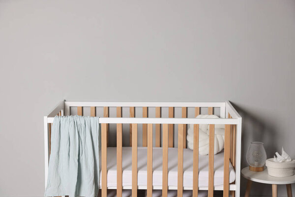 Детская кроватка и стол возле светло-серой стены, место для текста. Стильный интерьер детской комнаты