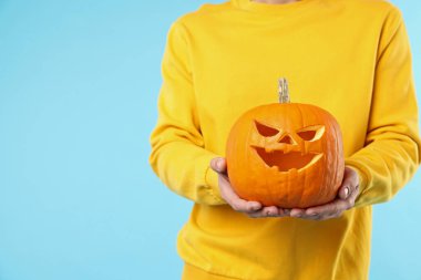 Cadılar Bayramı kutlaması. Açık mavi arka planda oyulmuş ürkütücü yüzlü balkabağı tutan adam, yakın plan. Metin için boşluk