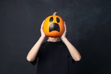 Cadılar Bayramı kutlaması. Siyah arka planda çizilmiş ürkütücü yüzlü balkabağı tutan çocuk dumanlı