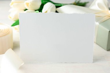 Boş kart, hediye ve çiçekler beyaz ahşap masada, yakın plan. Tasarım için model