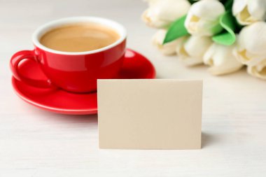 Boş kart, çiçekler ve beyaz ahşap masada bir fincan kahve, yakın plan. Tasarım için model