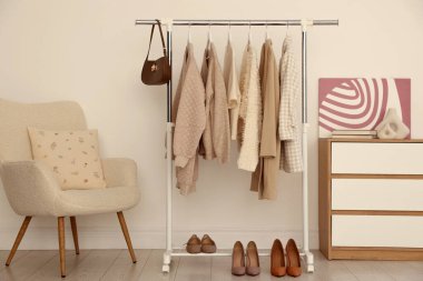 Farklı giysiler askıda, ayakkabılar ve çantalar kapalı alanda duvarda asılı.