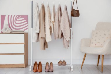 Farklı giysiler askıda, ayakkabılar ve çantalar kapalı alanda duvarda asılı.