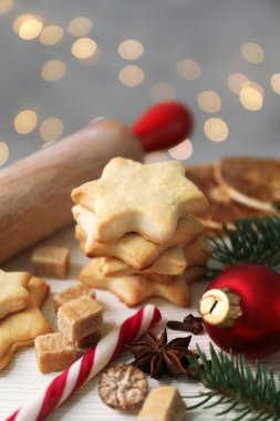 Yıldızlar, baharatlar, takılar ve köknar dalları şeklinde kurabiyeler içeren Noel kompozisyonu açık ahşap masa üzerinde gri arkaplan, bulanık ışıklar, yakın çekim