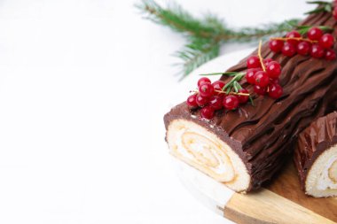 Lezzetli Noel kütüğü (geleneksel Noel pastası) beyaz fayanslı masa üzerinde kırmızı frenk üzümü, yakın plan. Metin için boşluk