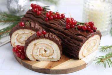 Lezzetli Noel kütüğü (geleneksel Noel pastası) kırmızı üzümlü ve köknar ağacı dallı beyaz masa, yakın plan