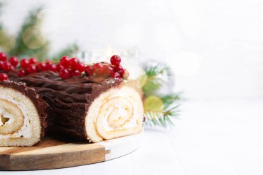 Lezzetli Noel kütüğü (geleneksel Noel pastası) beyaz fayanslı masa üzerinde kırmızı frenk üzümü, yakın plan. Metin için boşluk