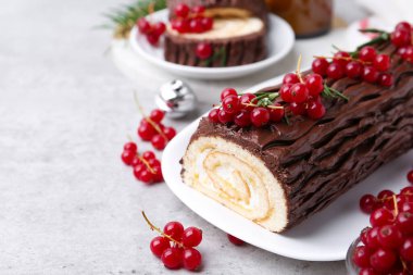 Lezzetli Noel kütüğü (geleneksel Noel pastası) gri desenli masa üzerinde kırmızı frenk üzümü, yakın plan. Metin için boşluk