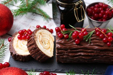 Lezzetli Noel kütüğü (geleneksel Noel pastası) kırmızı frenk üzümü, dekor ve köknar ağacı dalları ile masada, yakın plan