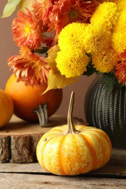 Sonbahar atmosferi. Üzerinde güzel çiçekler, yapraklar ve balkabakları olan vazolar kahverengi arka planda, yakın plan.