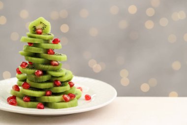 Kivi ve nar tohumlarından yapılmış Noel ağacı bej masadaki ışık arka planına karşı bulanık ışıklarla, yazı için yer. Bokeh etkisi