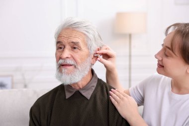 Bakıcı, kıdemli adamın evde işitme cihazı takmasına yardım ediyor.