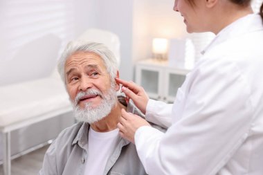 Doktor hastanede yaşlı adamın kulağına işitme cihazı takıyor.