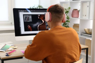 Kulaklıklı profesyonel rötuş cihazı. Ofisteki bilgisayarda fotoğraf düzenleme işi. Arka plan.