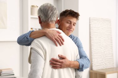 Baba ve oğul evde birbirlerine sarılıyorlar.