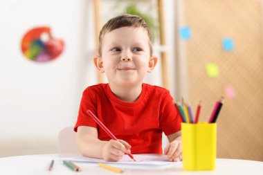 Beyaz masada renkli kalemler çizen sevimli küçük bir çocuk.