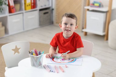 Beyaz masa içinde keçeli kalemle çizim yapan komik çocuk.