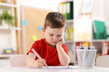 Beyaz masaya keçeli kalemle çizen sevimli küçük çocuk.