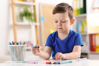 Beyaz masaya keçeli kalemle çizen sevimli küçük çocuk.