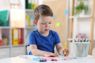 Beyaz masaya keçeli kalemle çizen sevimli küçük çocuk.