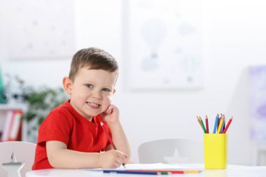 Beyaz masa içinde renkli kalemler çizen komik küçük çocuk. Metin için boşluk