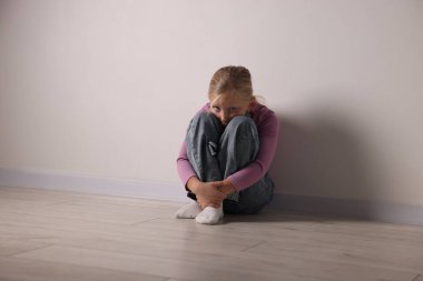 Beyaz duvarın yanındaki üzgün küçük kız.