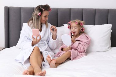 Bornozlu bir anne ve kızı evde makyajlarını yapıyor.