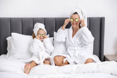 Havlu ve salatalık dilimli bornozlu bir anne ve kız evde yataktalar.