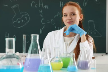 Okula dönelim. Kimyasal formüllü karatahtaya karşı masanda sıvı dolu mataralarla duran bir kız.