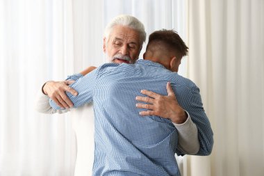 Baba ve oğul evde birbirlerine sarılıyorlar.