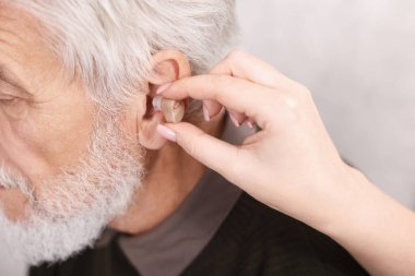 Bakıcı, kıdemli adamın evde işitme cihazı takmasına yardım ediyor.