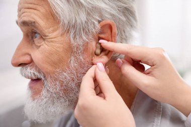 Doktor hastanede yaşlı adamın kulağına işitme cihazı takıyor.