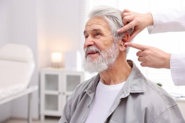 Doktor hastanede yaşlı adamın kulağına işitme cihazı takıyor.