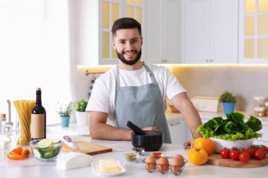 Mutfaktaki masada yemek pişiren gülümseyen adam.