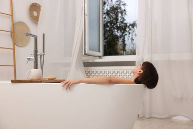 Kadın açık pencereli banyoda banyo yapıyor.