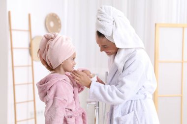 Anne banyoda kızının yüzüne krem sürüyor.