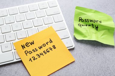 Şifre değiştiriliyor. Gri masadaki bilgisayar klavyesinin yanında eski ve yeni parolaları olan yapışkan notalar, yakın plan