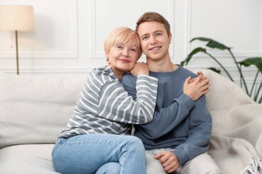 Anne ve oğul evdeki kanepede kucaklaşıyorlar.