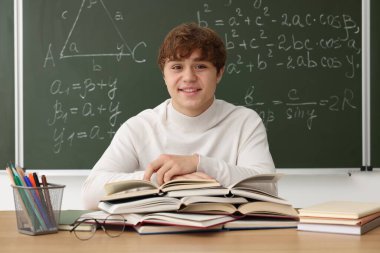 Okula dönelim. Ahşap masada kitap ve kırtasiye malzemesi olan öğrenci içeride matematik ödevi olan karatahtaya karşı.