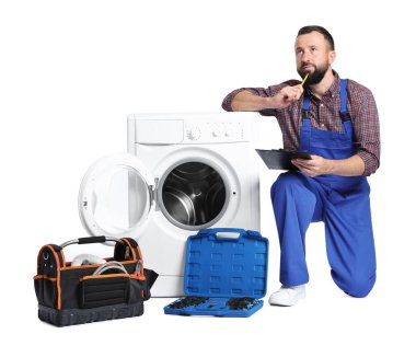 Beyaz arka planda bozuk çamaşır makinesinin yanında panosu olan profesyonel bir tamirci.