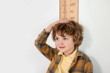 Boyunu beyaz duvarın yanında çizelgeyle ölçen küçük çocuk.