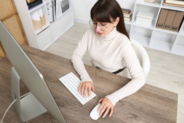 Ofisteki bilgisayarda çalışan genç bir kadın.