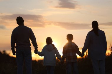 Aile gün batımında, arka planda el ele tutuşuyor.