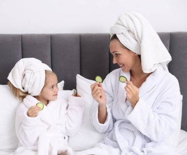 Havlu ve salatalık dilimli bornozlu bir anne ve kız evde yataktalar.