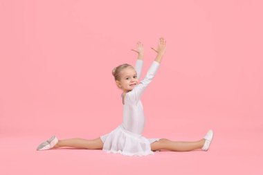 Gülümseyen küçük kız pembe arka planda jimnastik yapıyor.